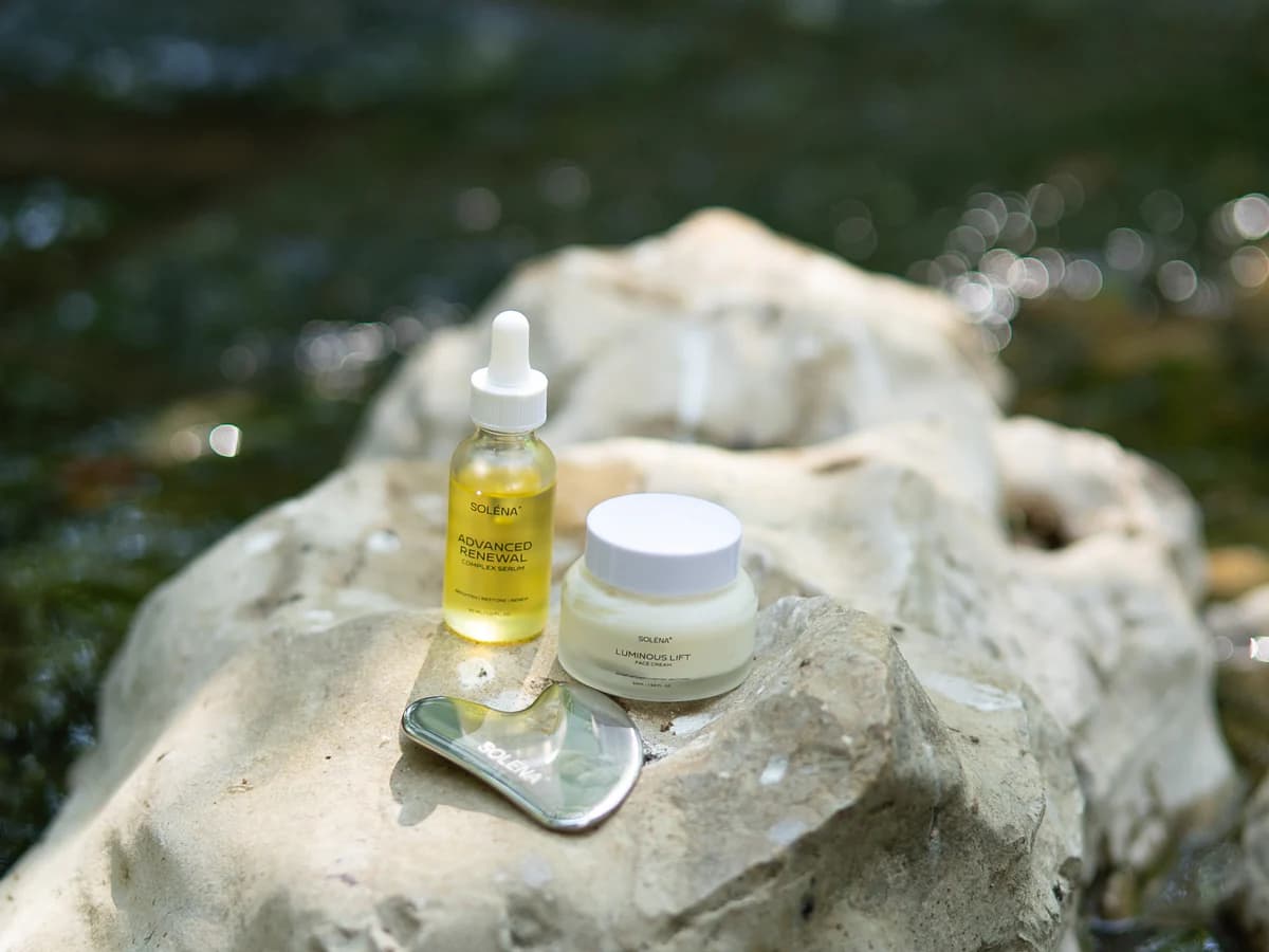 SOLÉNA serum, face cream and gua sha beside a stream