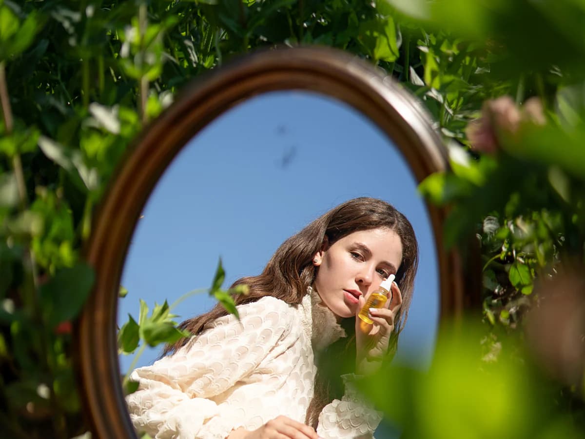 A woman holding Soléna serum beside a garden mirror